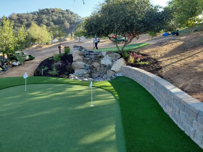 A backyard putting green with a rock cascade and block border.