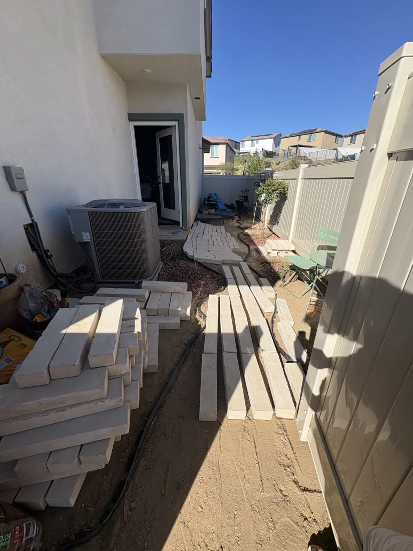 Before: Side yard before completion of the paver walkway, with pavers staged beside the house.